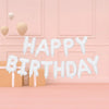A decorative banner spelling HAPPY BIRTHDAY made of white fluffy letters hangs against a pink wall with rose gold foil balloo
