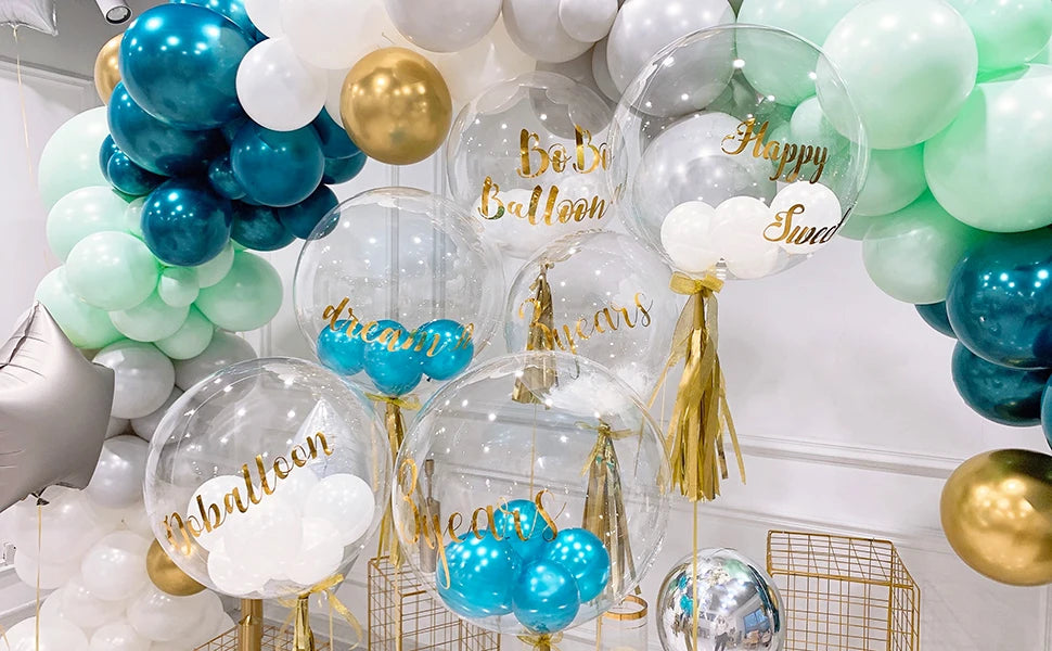 A collection of clear and iridescent bubble balloons in shades of blue, green, and gold for party decoration.