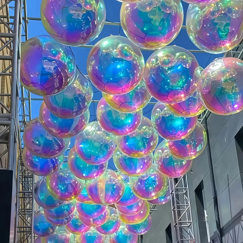 A cluster of metallic rainbow foil balloons reflecting iridescent colors, suspended in an indoor setting.