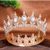 A gold crystal rhinestone crown topper displayed on a wooden surface.