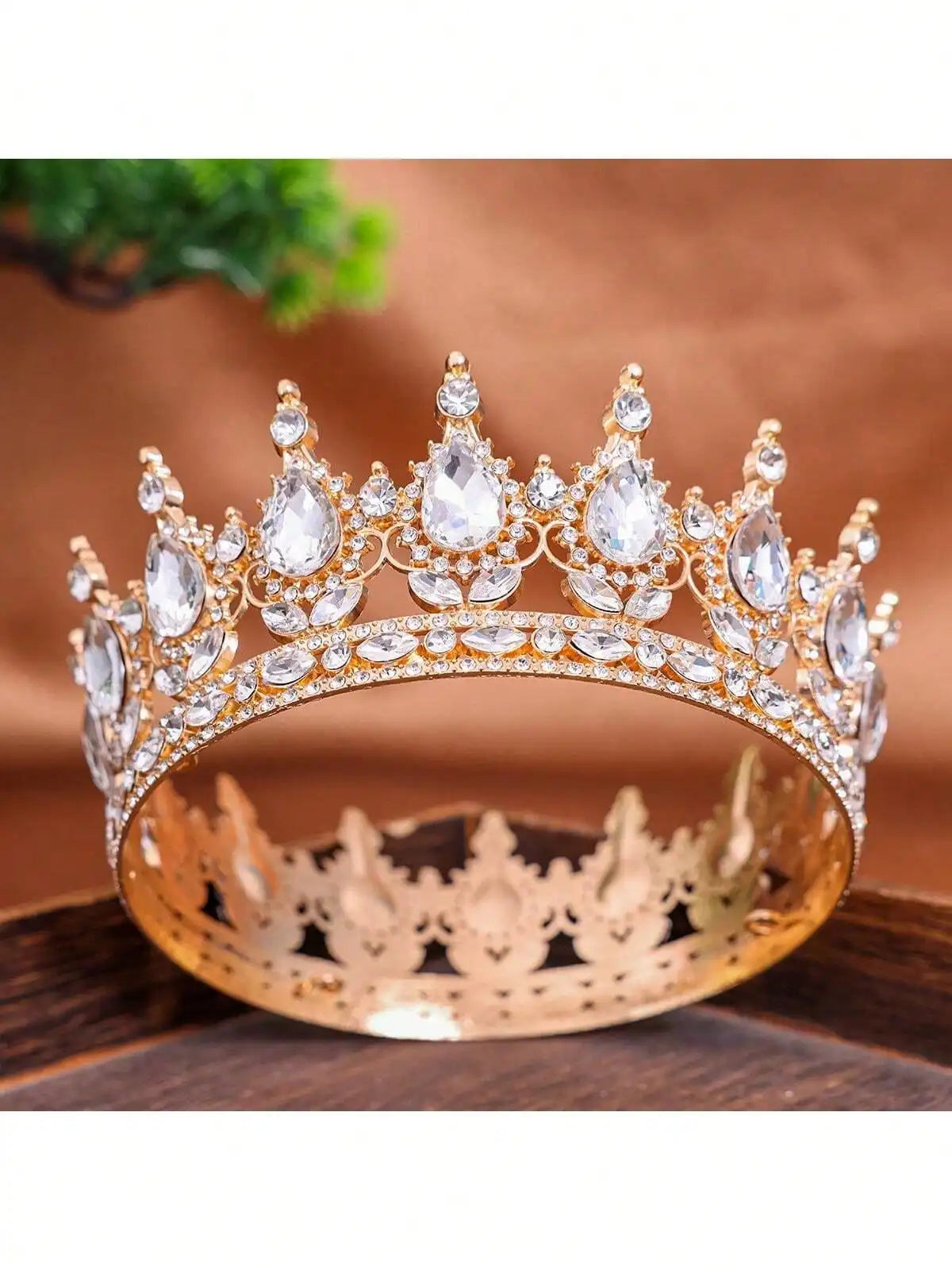 A gold crystal rhinestone crown topper displayed on a wooden surface.