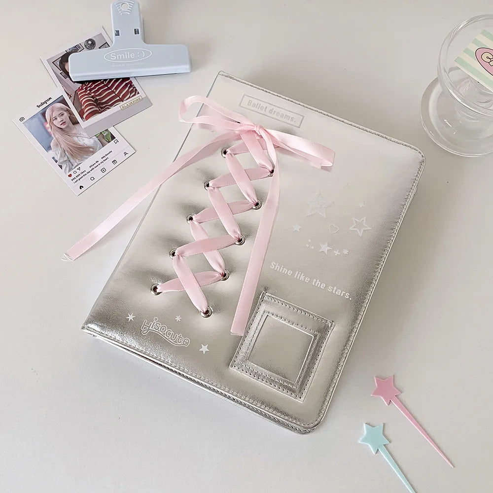 A silver leather photo album with a pink ribbon closure and star embellishments is displayed on a white surface.