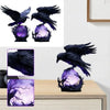 Gothic raven sculpture with purple glow illuminating a dark branch on a wooden surface.