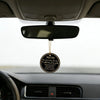 A black prayer tag hangs from the rearview mirror inside a car, featuring Arabic and English text.