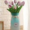 A bouquet of six artificial purple and pink tulips in a light blue ceramic vase