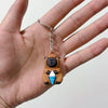 Un petit pendentif de clé USB en forme de capybara brun tenant une glace, suspendu à une chaîne argentée.