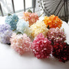 A collection of silk hydrangea stems in various shades of blue, pink, and orange arranged on a white surface.