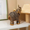 A vintage resin elephant ornament with intricate gold detailing sits on a white shelf.