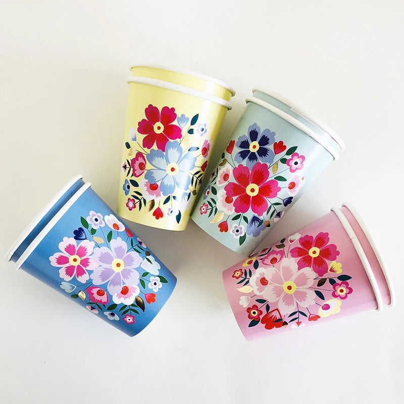 A set of five colorful floral disposable cups in shades of pink, blue, and yellow arranged on a white surface.
