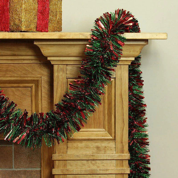 A festive Christmas tinsel garland with red and green strands is draped over a wooden mantelpiece.