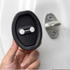 A hand holds a black silicone door lock protector with a silver latch mechanism against a white surface.