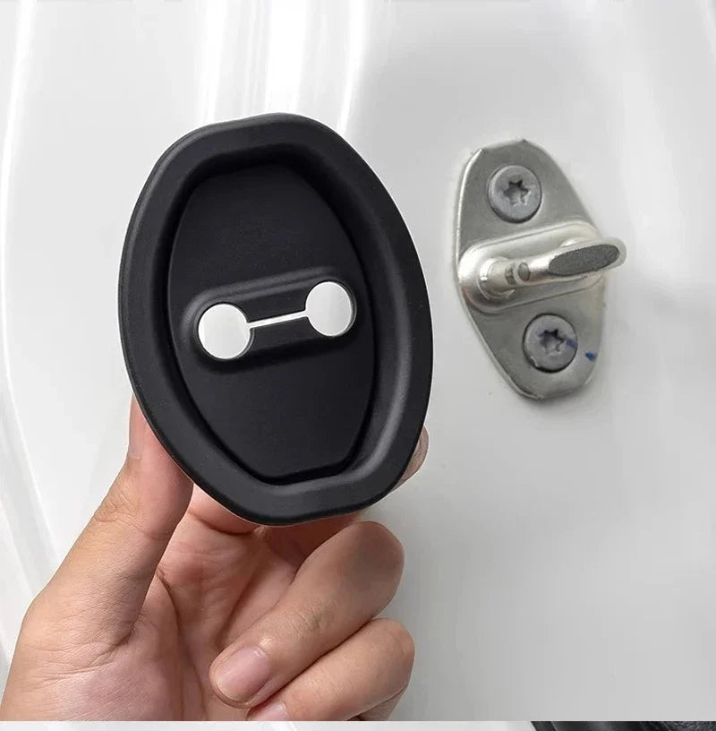 A hand holds a black silicone door lock protector with a silver latch mechanism against a white surface.