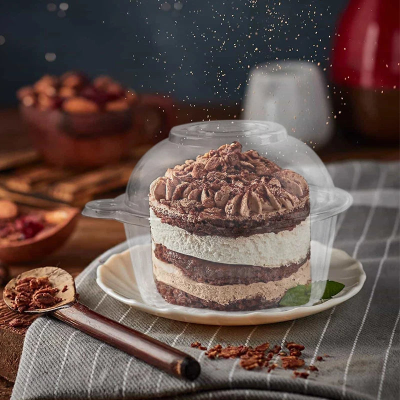 A layered chocolate and cream cupcake in a clear plastic cup with a lid, resting on a wooden surface.