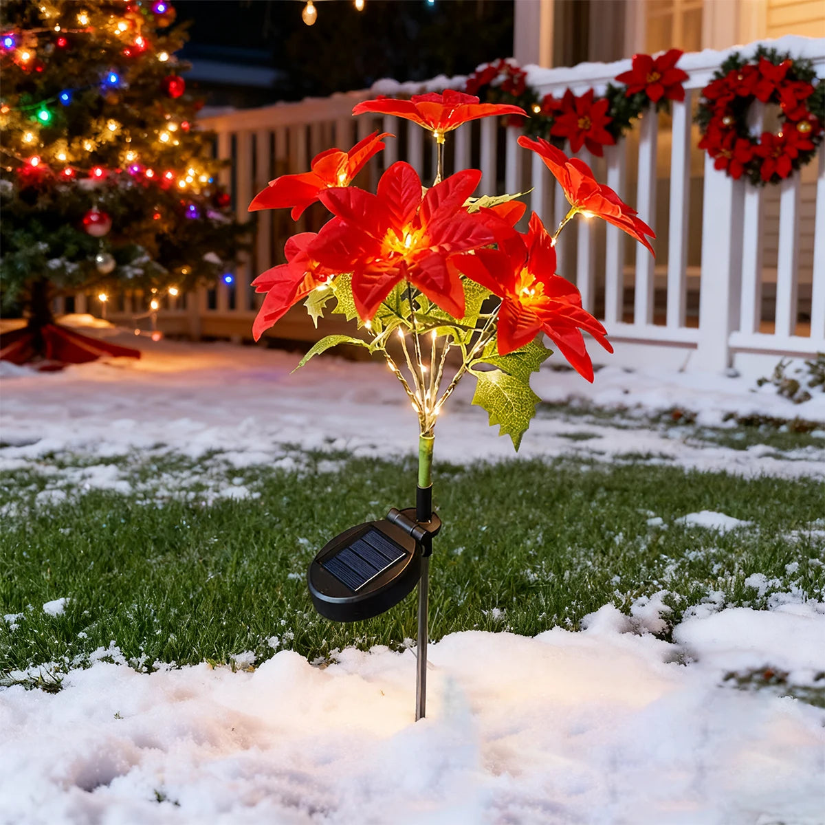 A vibrant red poinsettia flower illuminated by solar garden lights in a snowy outdoor setting.