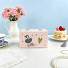 A pink ballet music box with a lid open, featuring a silhouette of a swan and a heart design, placed on a white table.