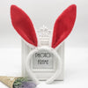 A pair of red bunny ear headbands with white fluffy ears displayed in a white picture frame.