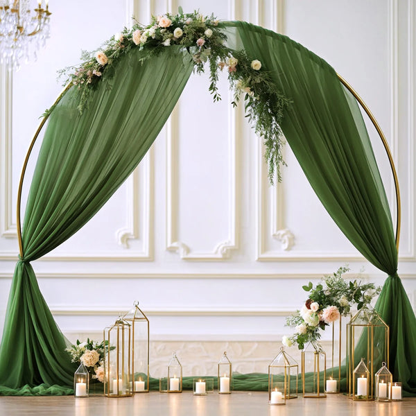 Elegant green chiffon arch drapes framing a white wall with floral greenery and gold accents