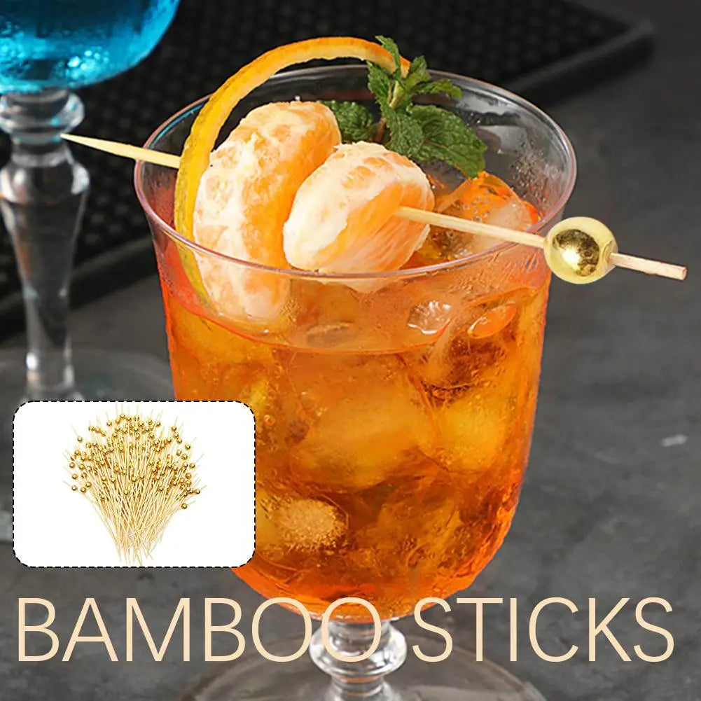 A glass of orange-colored cocktail with citrus fruit garnishes and bamboo sticks for serving.