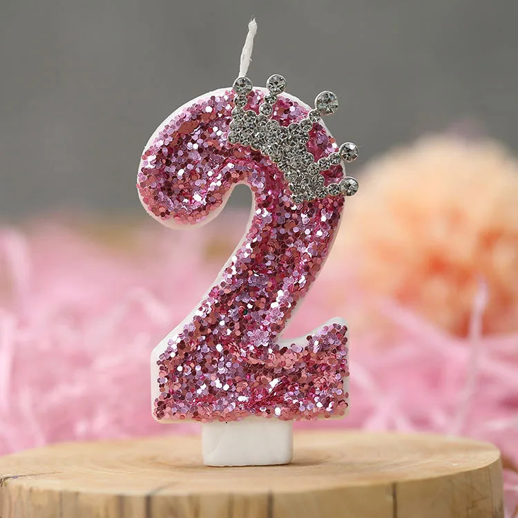A pink sequin number two candle with a silver crown topper on a white base.