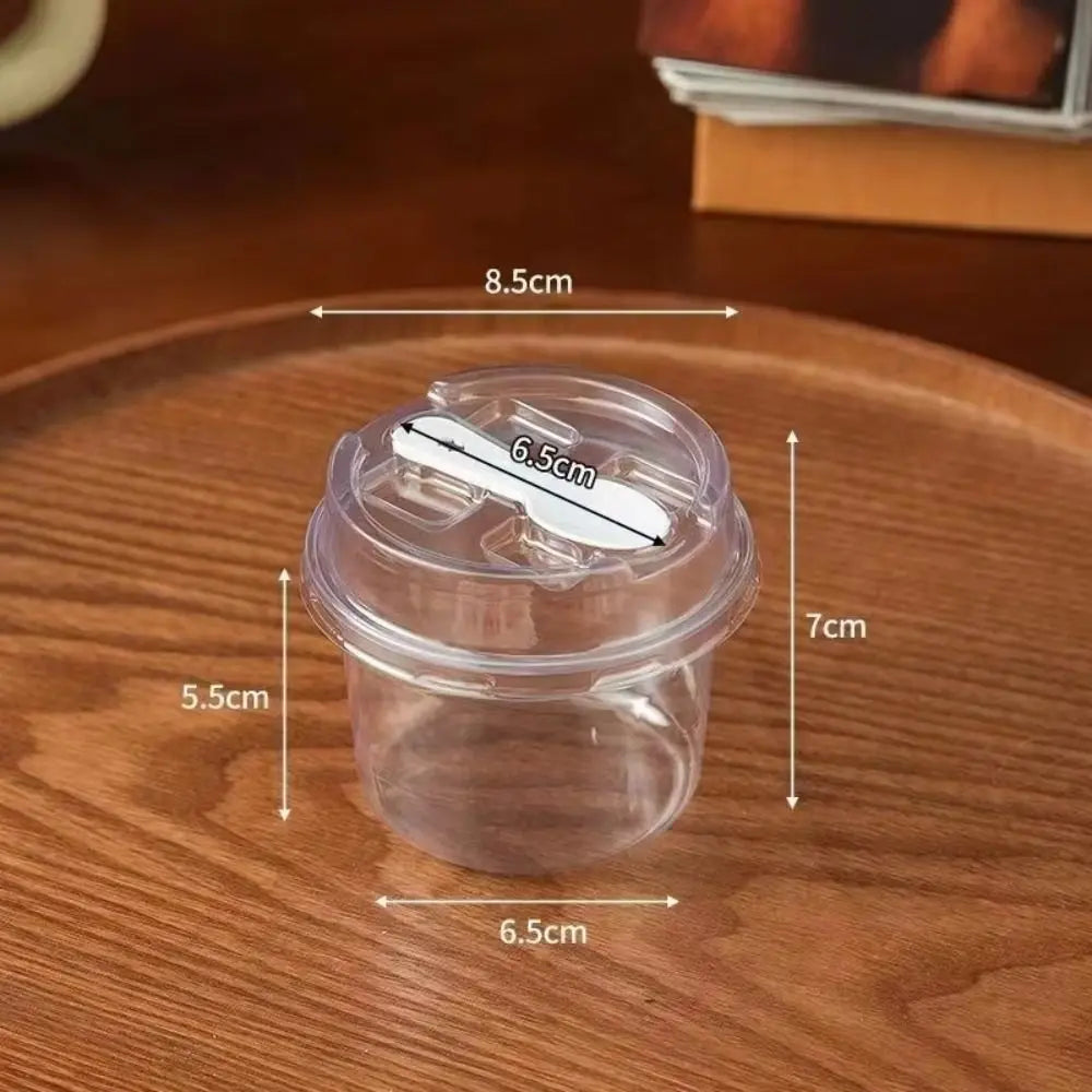 A clear disposable pudding cup with a lid and spoon shown on a wooden surface.