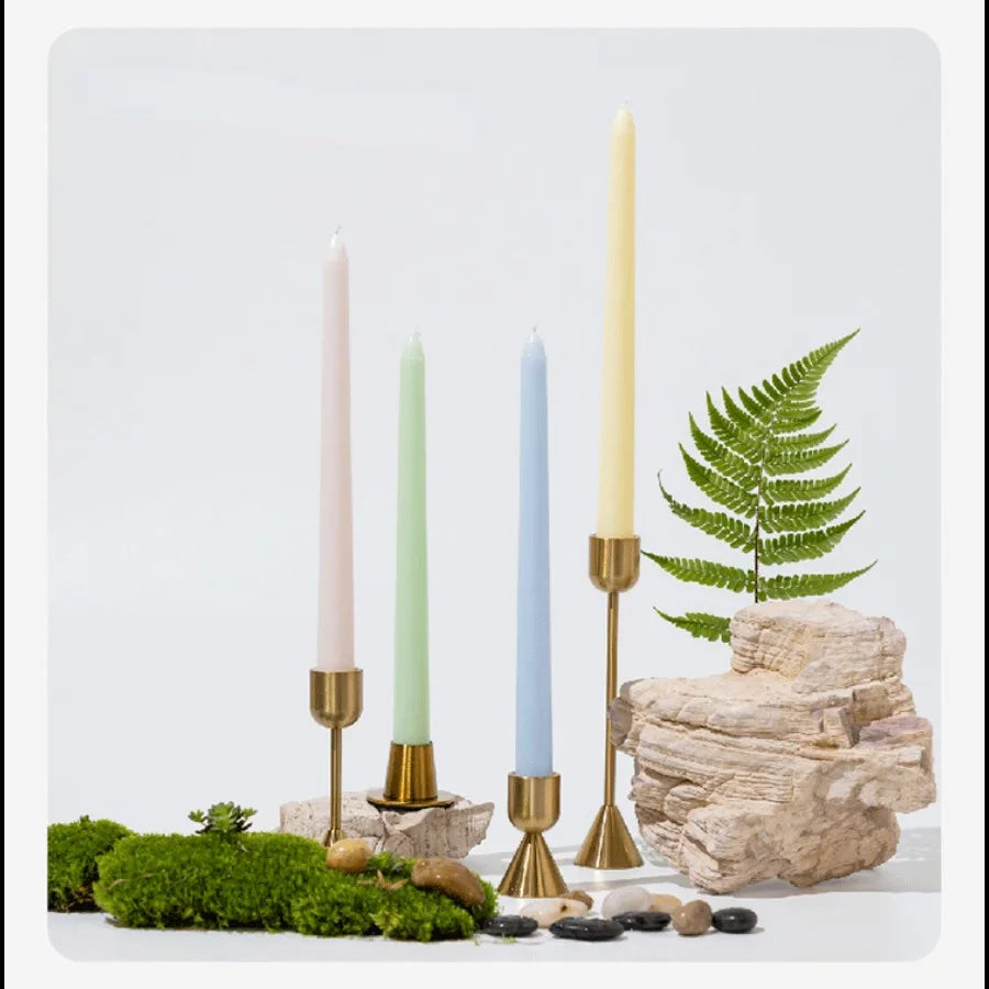 A collection of tall taper candles in gradient colors, including pink, green, and blue, displayed on natural wood and moss.