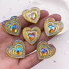 A hand holds a set of twelve heart-shaped AB black peacock resin rhinestone flatbacks.