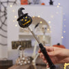 Une main tient une lanterne en bâton noire et lumineuse avec une tête de citrouille sculptée contre un fond blanc.