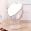 Espejo de maquillaje con forma de corazón blanco y marco decorativo sobre una superficie de madera.