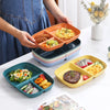 A set of colorful, multi-compartment portion control plates is displayed on a white table with food items.