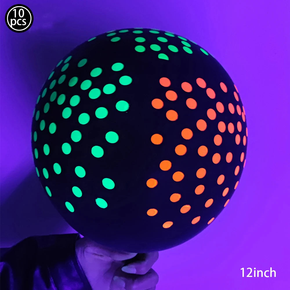 A hand holds a large, dark latex balloon covered in bright neon green and orange glow-in-the-dark dots against a purple backg