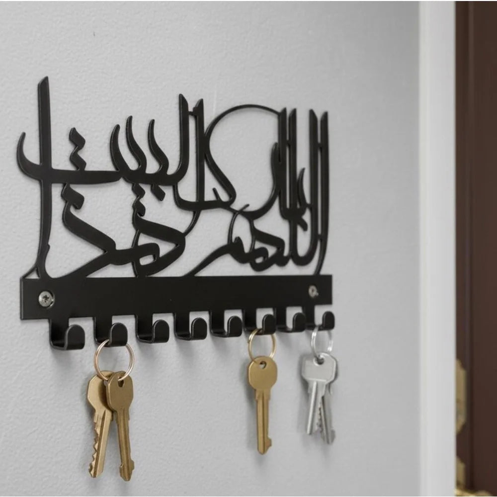 Black Islamic Arabic blessing key holder with hooks and brass keys mounted on a white wall.