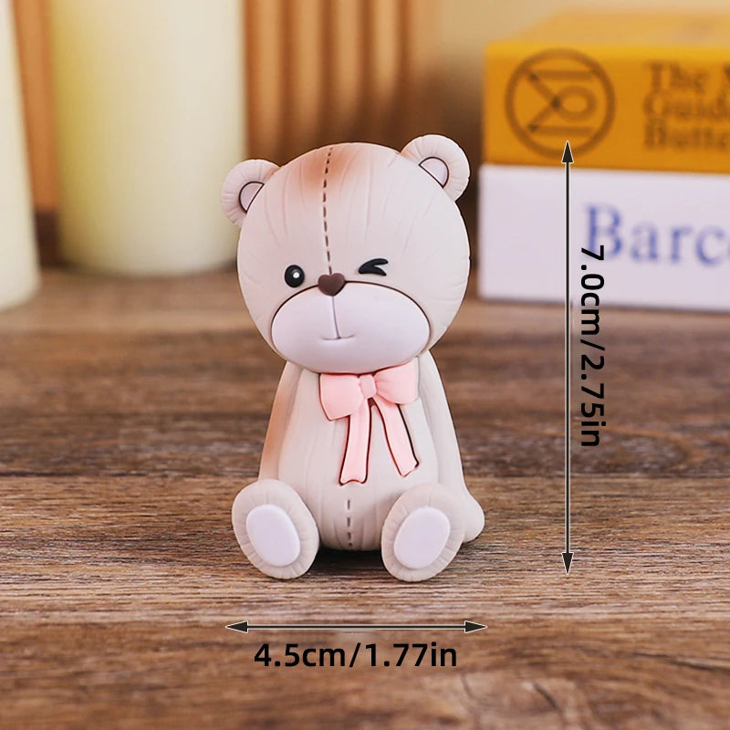 A light pink baby block cake topper shaped like a cute bear with a bow, shown on a wooden surface.