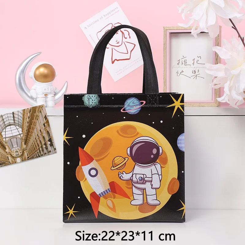 A black tote bag featuring a yellow sun design with an astronaut and a rocket, set against a pink background.