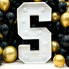A large white marquee light-up letter shaped like the number 5 displayed against a dark background of balloons.