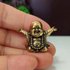 A small brass statue of a laughing Buddha with expressive features held in a person's hand.
