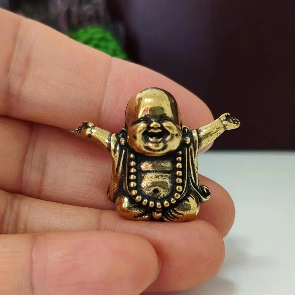 A small brass statue of a laughing Buddha with expressive features held in a person's hand.