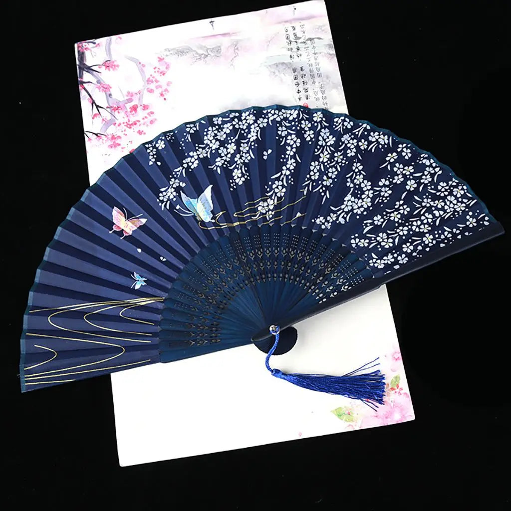 A dark blue silk folding fan decorated with white floral patterns and gold accents, shown against a light background.