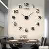 A modern wall clock with black numbers and hands is mounted on a white wall above a dining table.