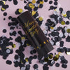 A black tube of Hand Twist Confetti Cannons lying on a pink surface surrounded by scattered black and gold confetti.