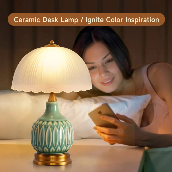 A ceramic desk lamp with a green crackle glaze sits on a table next to a woman using a smartphone.