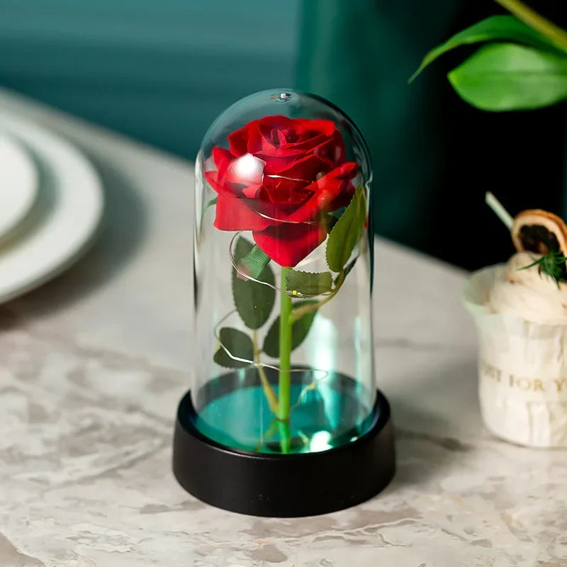 Ein Glasvase hält eine leuchtend rote Rose mit grünem Stiel, beleuchtet von einer LED in einer schwarzen Basis.
