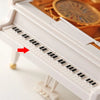 A close-up view of a white hand-crank music box with a visible piano keyboard and a spinning ballerina inside.