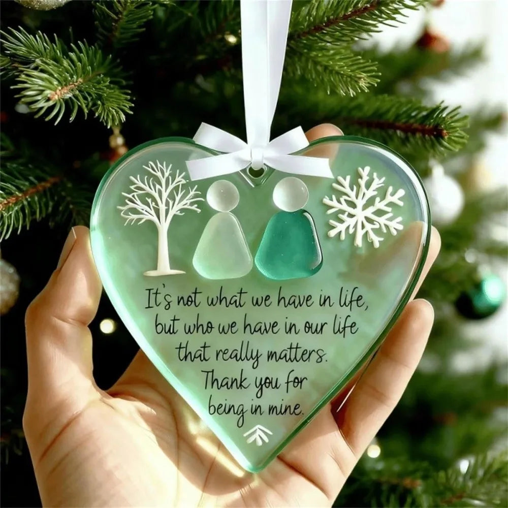 A handcrafted acrylic friendship snowflake Christmas pendant with two silhouette figures is held against a green Christmas tr
