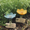 A wooden sign labeled Cups for Bee is placed in the dirt among green plants.