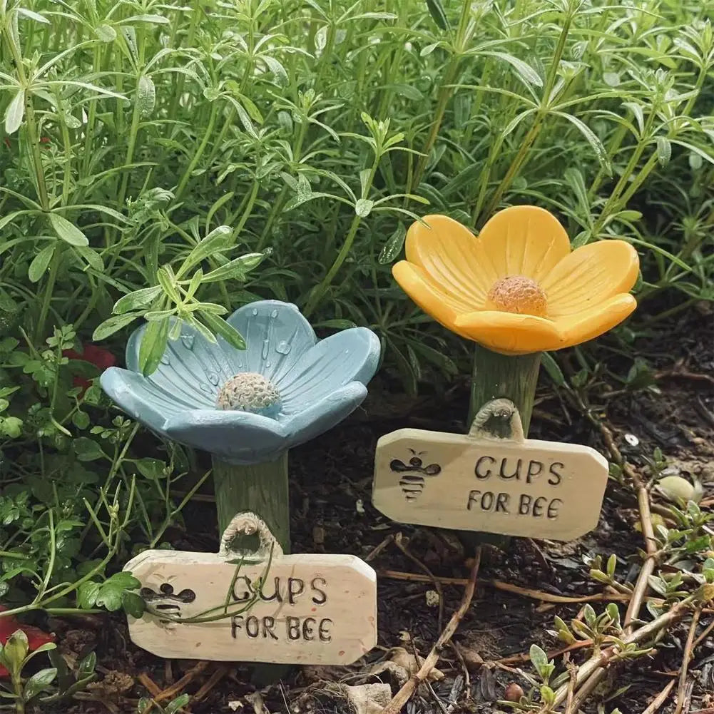 A wooden sign labeled Cups for Bee is placed in the dirt among green plants.
