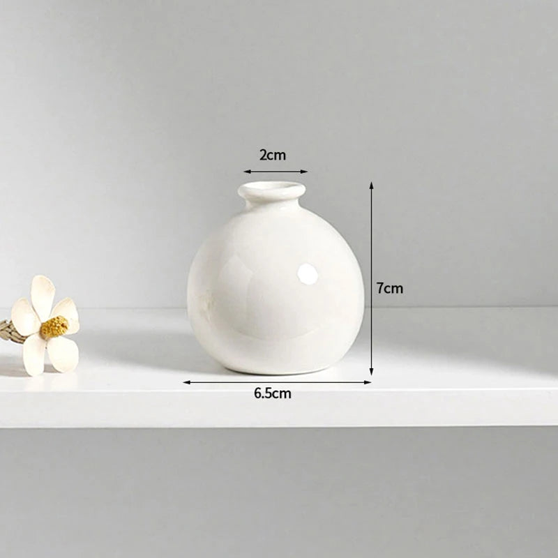 A white ceramic mini vase with a rounded body and a small opening, shown on a white surface.