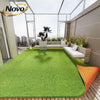 Artificial grass carpet laid out on a wooden deck with modern glass architecture and potted plants.