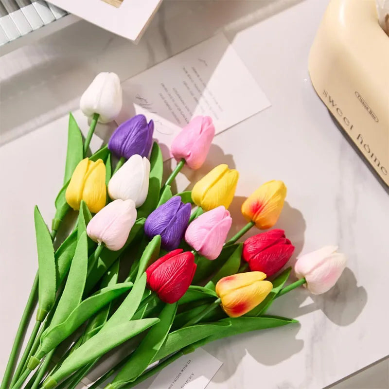 A bouquet of realistic artificial tulips in shades of white, yellow, pink, and purple arranged on a white surface.