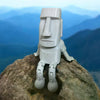 A 3D printed Moai statue figurine with movable joints carved from light gray stone, standing on a large rock against a blue m