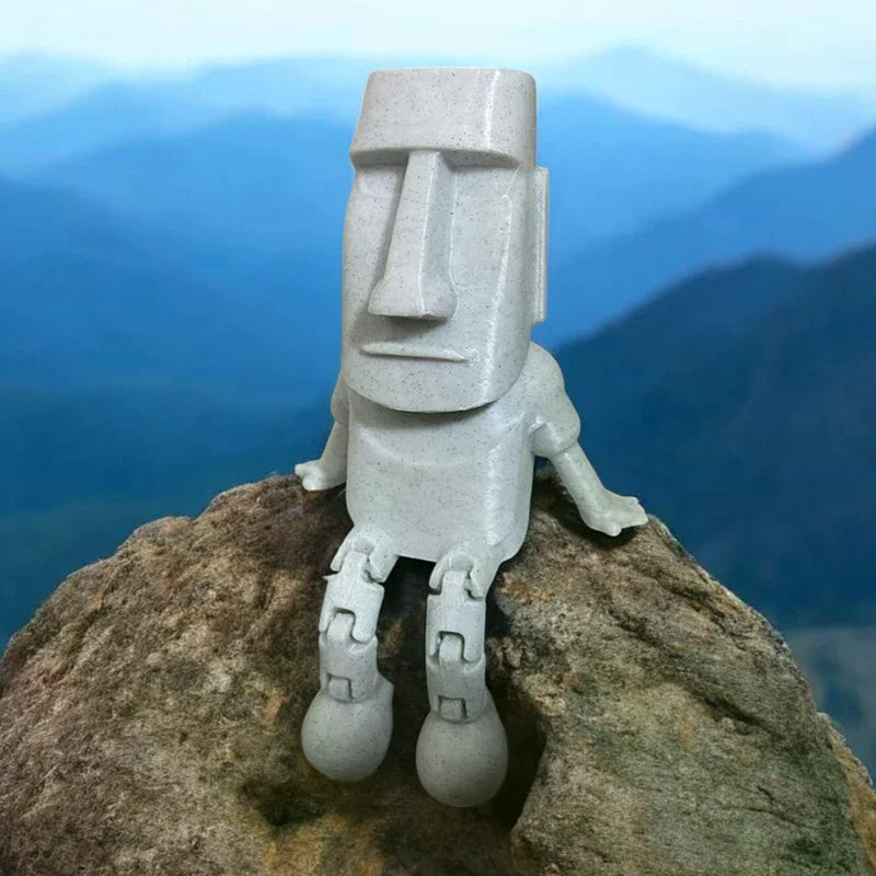 A 3D printed Moai statue figurine with movable joints carved from light gray stone, standing on a large rock against a blue m